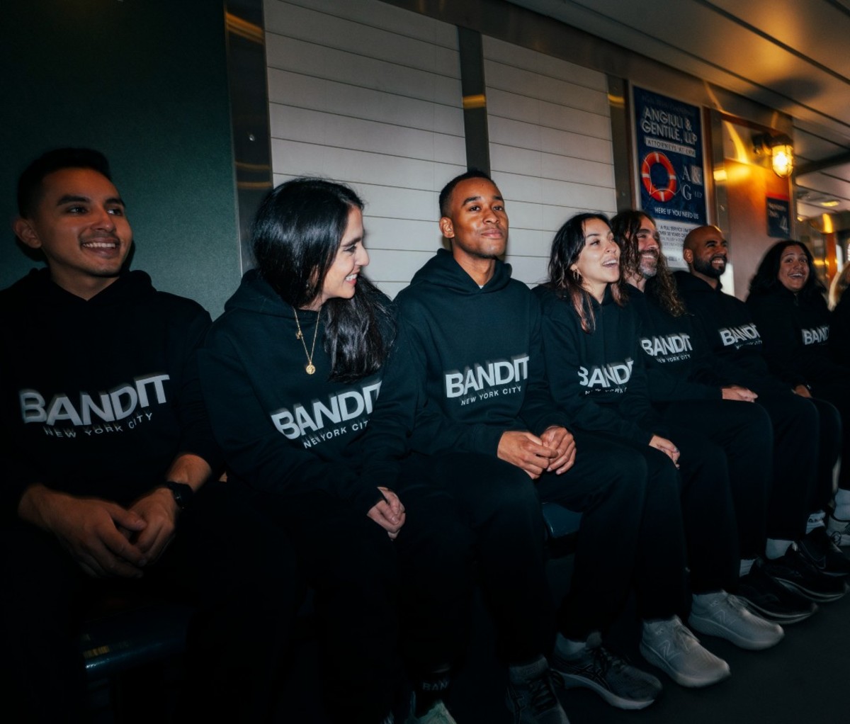 Men and women sitting on bench wearing black sweatsuits that say Bandit Running