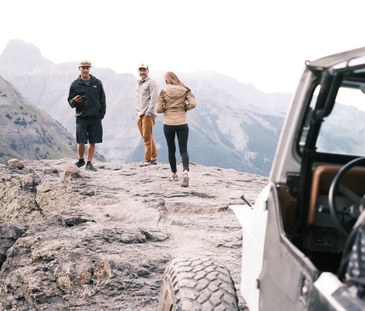 Two men and woman walking away from Jeep and exploring hike vista