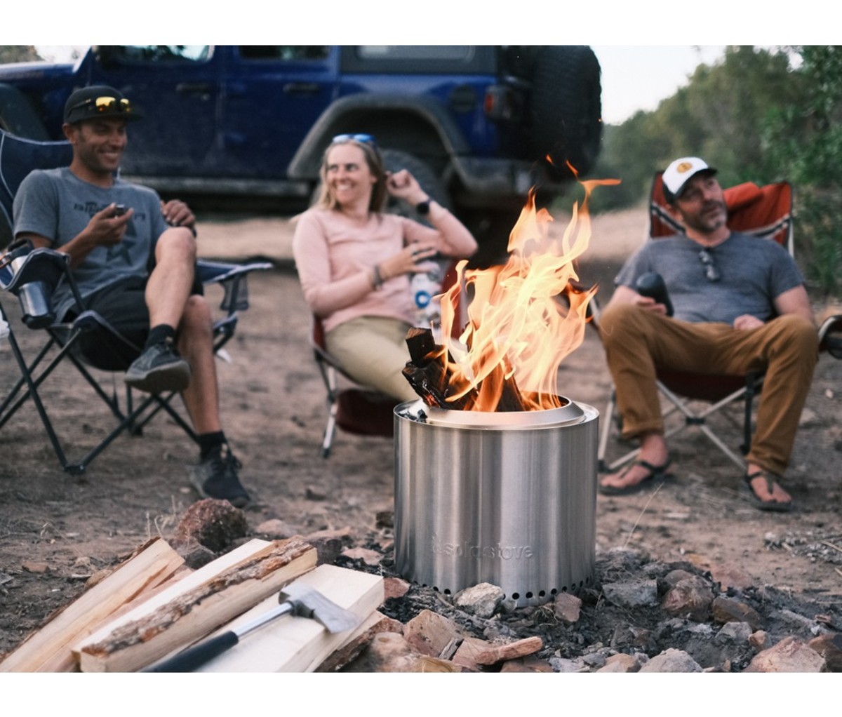 Two man and woman sitting around fire at campsite