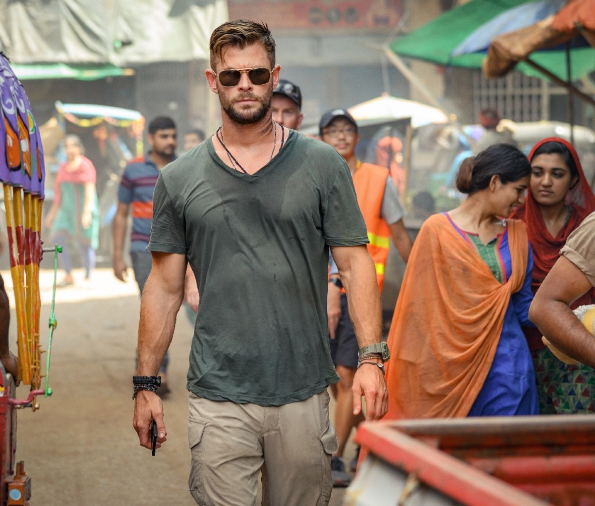 Chris Hemsworth in Sonnenbrille und T0shirt geht während einer Szene aus „Extraction“ durch einen Markt.
