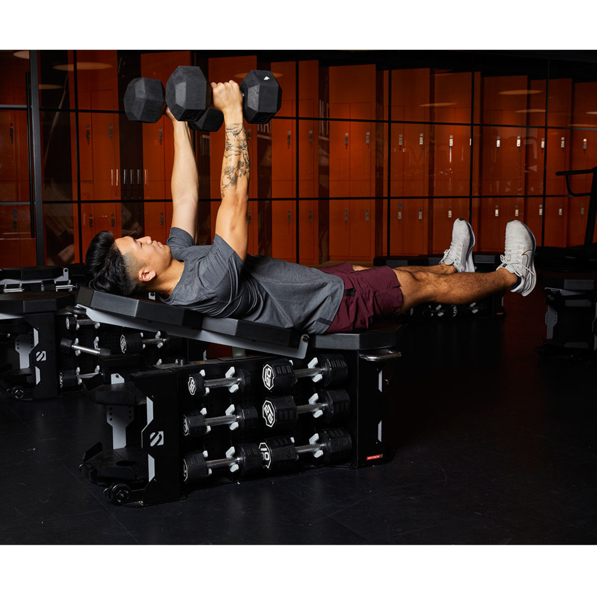 Athletic man wearing gray t-shirt and maroon shorts doing incline barbell chest press with legs raised 