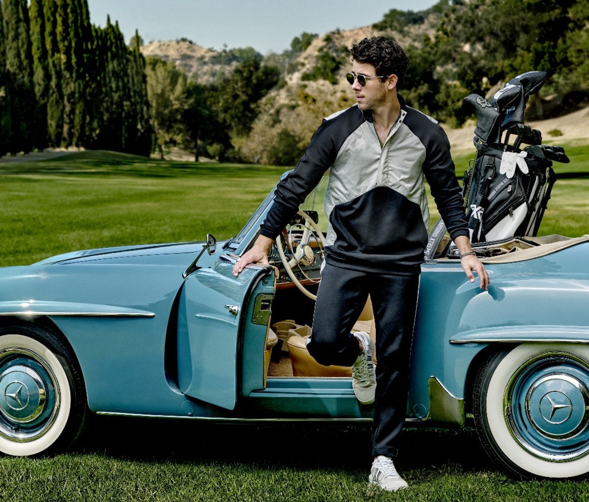 Actor Nick Jonas stepping out of blue vintage sports car on golf course