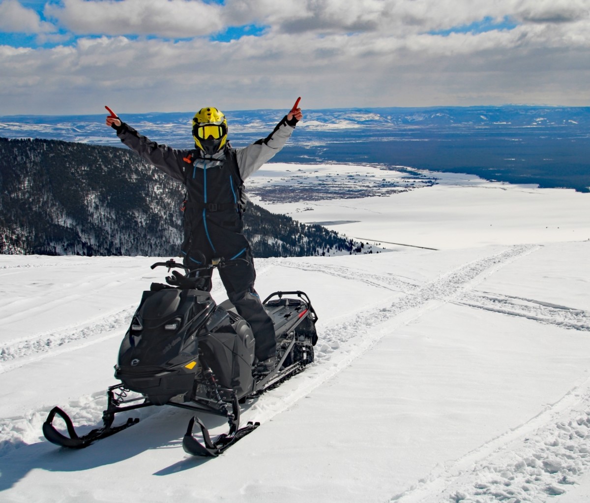 Man standing with arms raised on a snowmobile on top of a mountain plateau