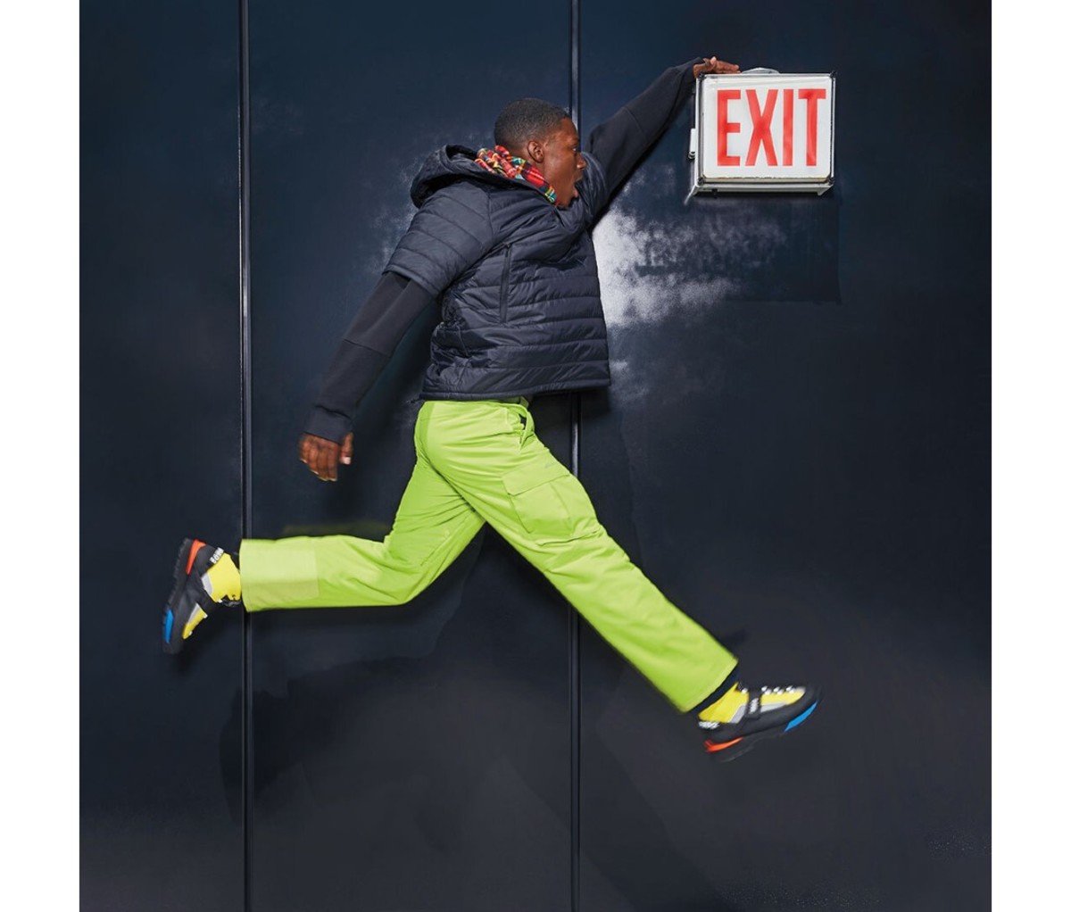 A man wearing a puffer coat jumps up to touch an Exit sign.