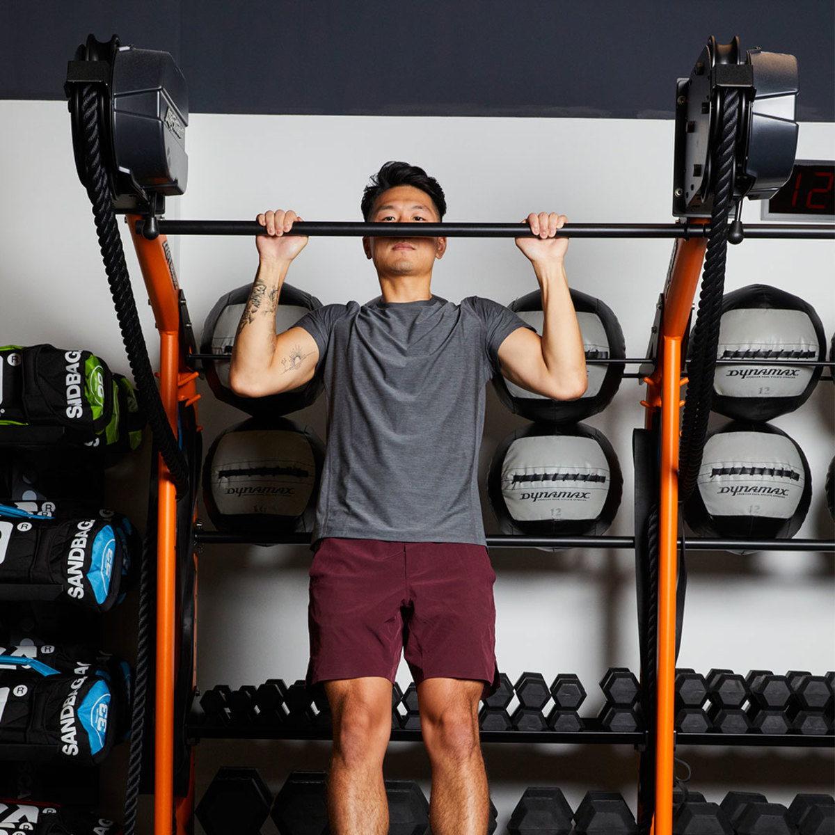 Athletic man in gray t-shirt and maroon shorts doing pull-up