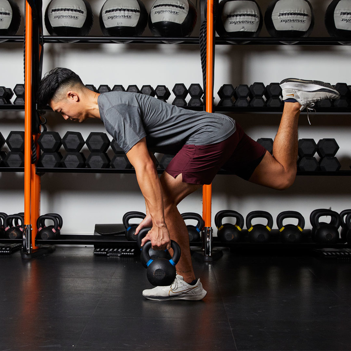 Athletic man in gray t-shirt and maroon shorts doing single leg romanian deadlift