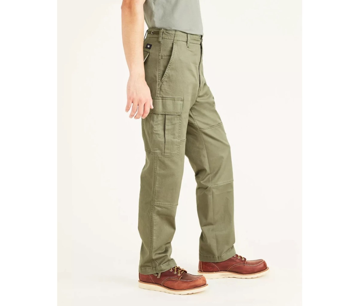 Man with grey t-shirt and green cargo pants and brown boots on an off-white background.