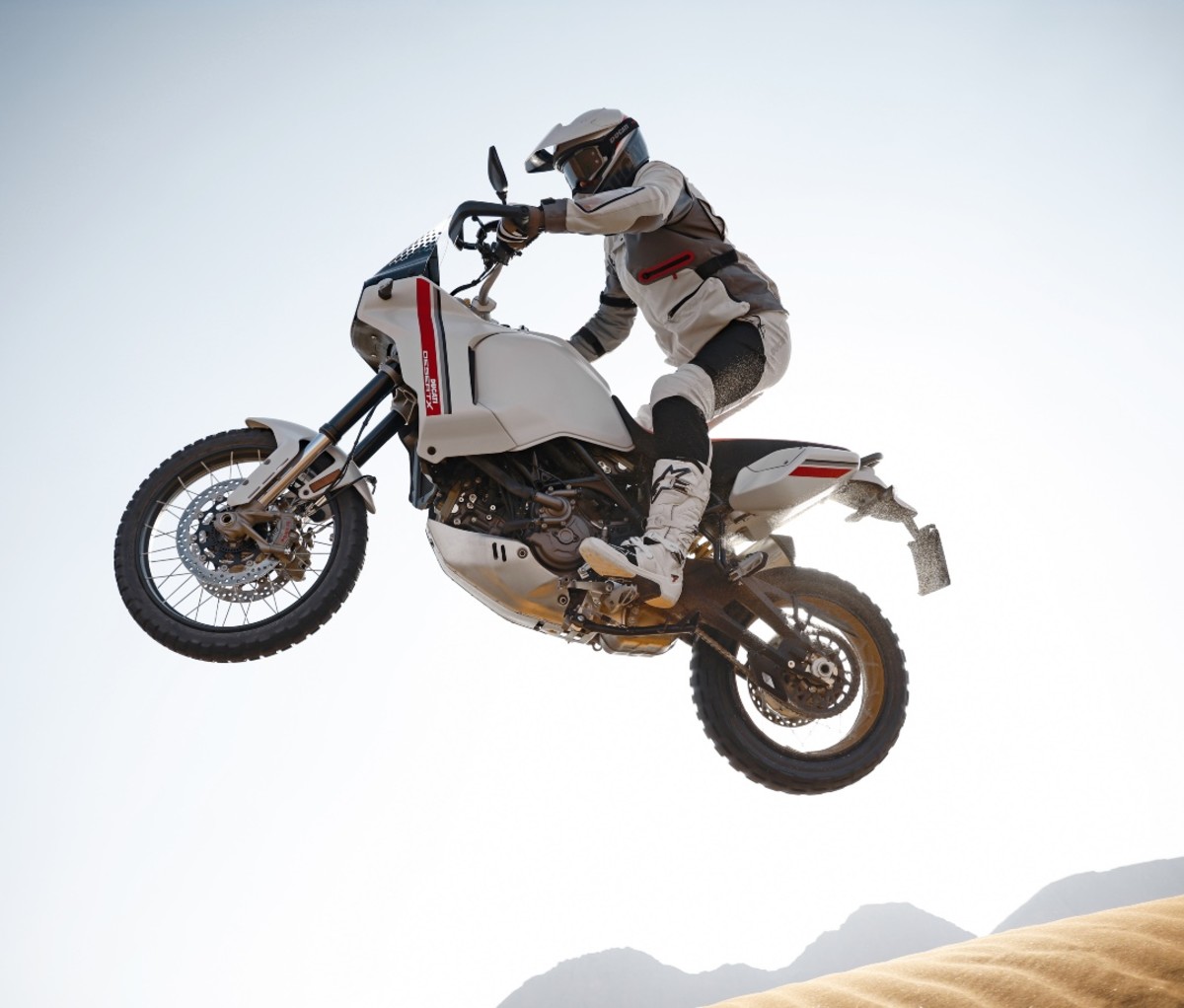 A motorcycle rider on an adventure bike jumping a sand dune.