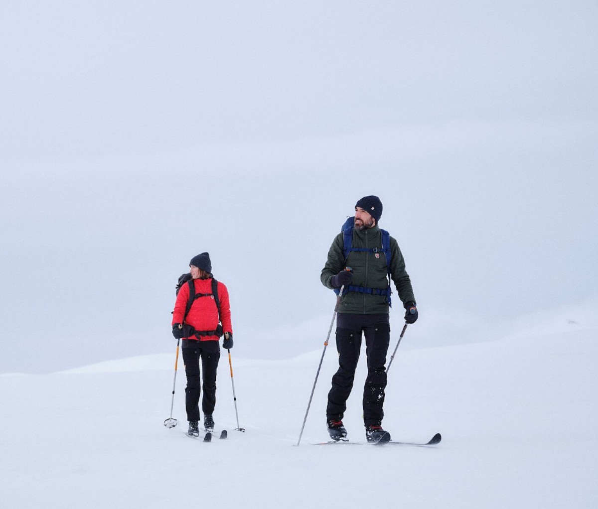 Woman in red jacket and man in green jacket cross country skiing