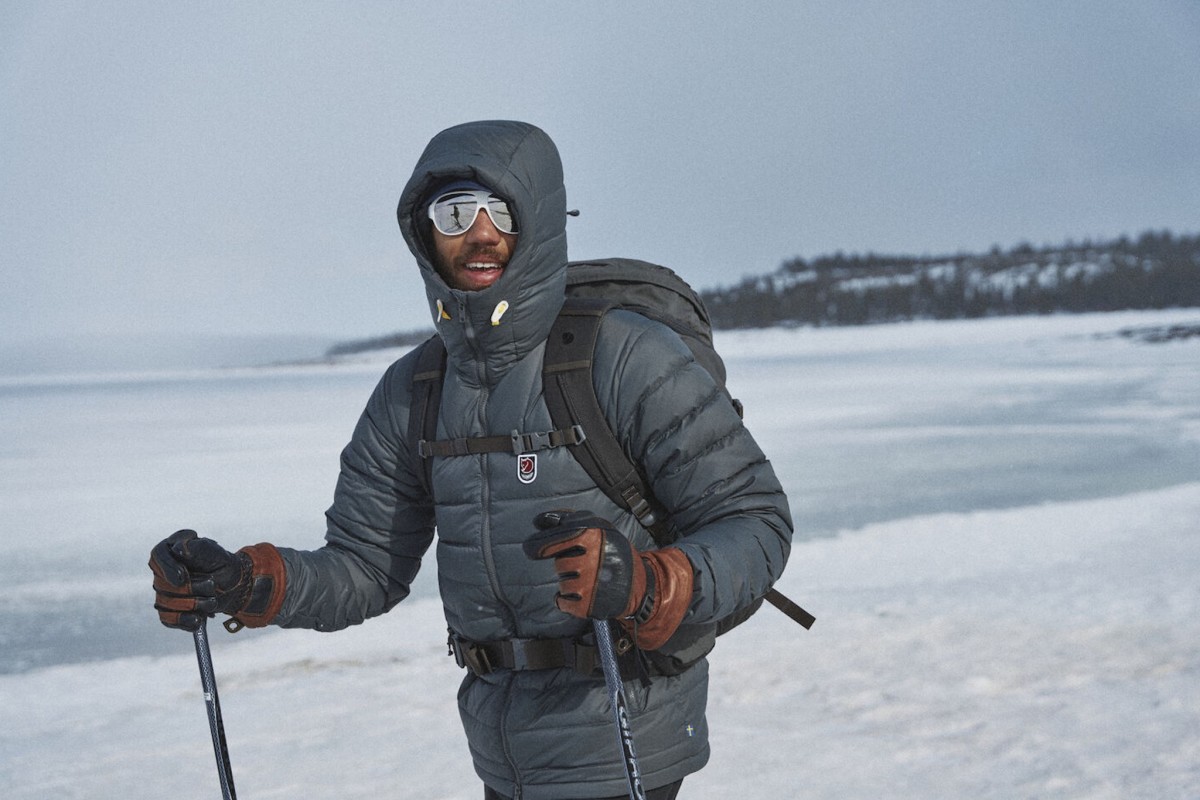 Adventurer wearing hooded down jacket and sunglasses with ski poles in snowy landscape