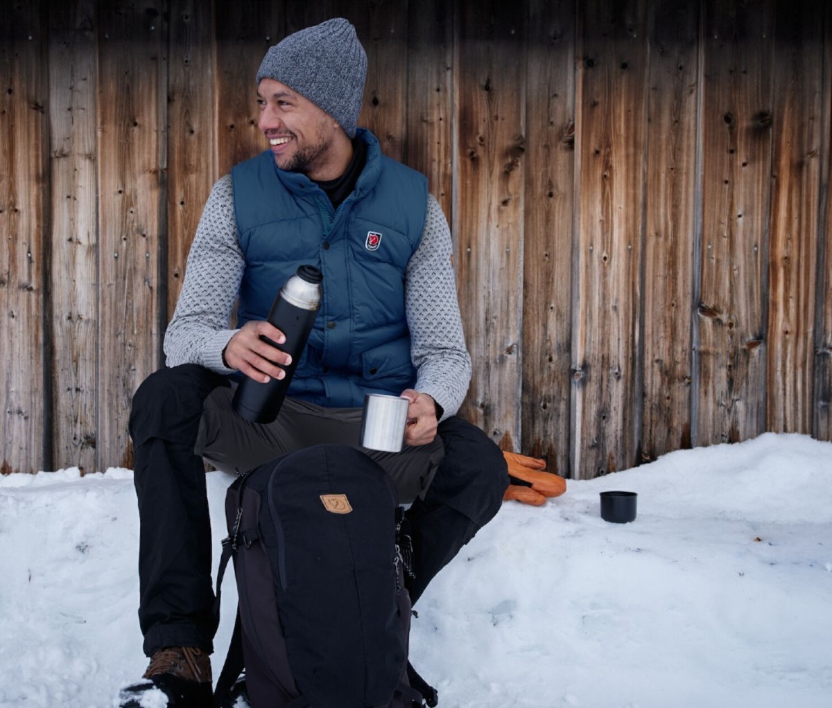 Man sitting in snow in vest and beanie