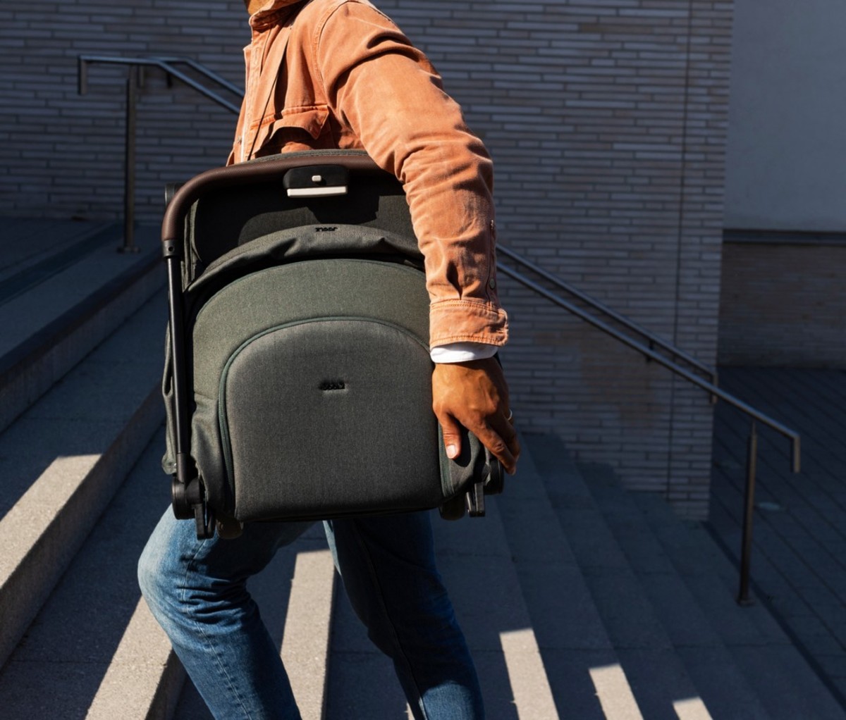 Man in orange jacket carrying green travel stroller over shoulder