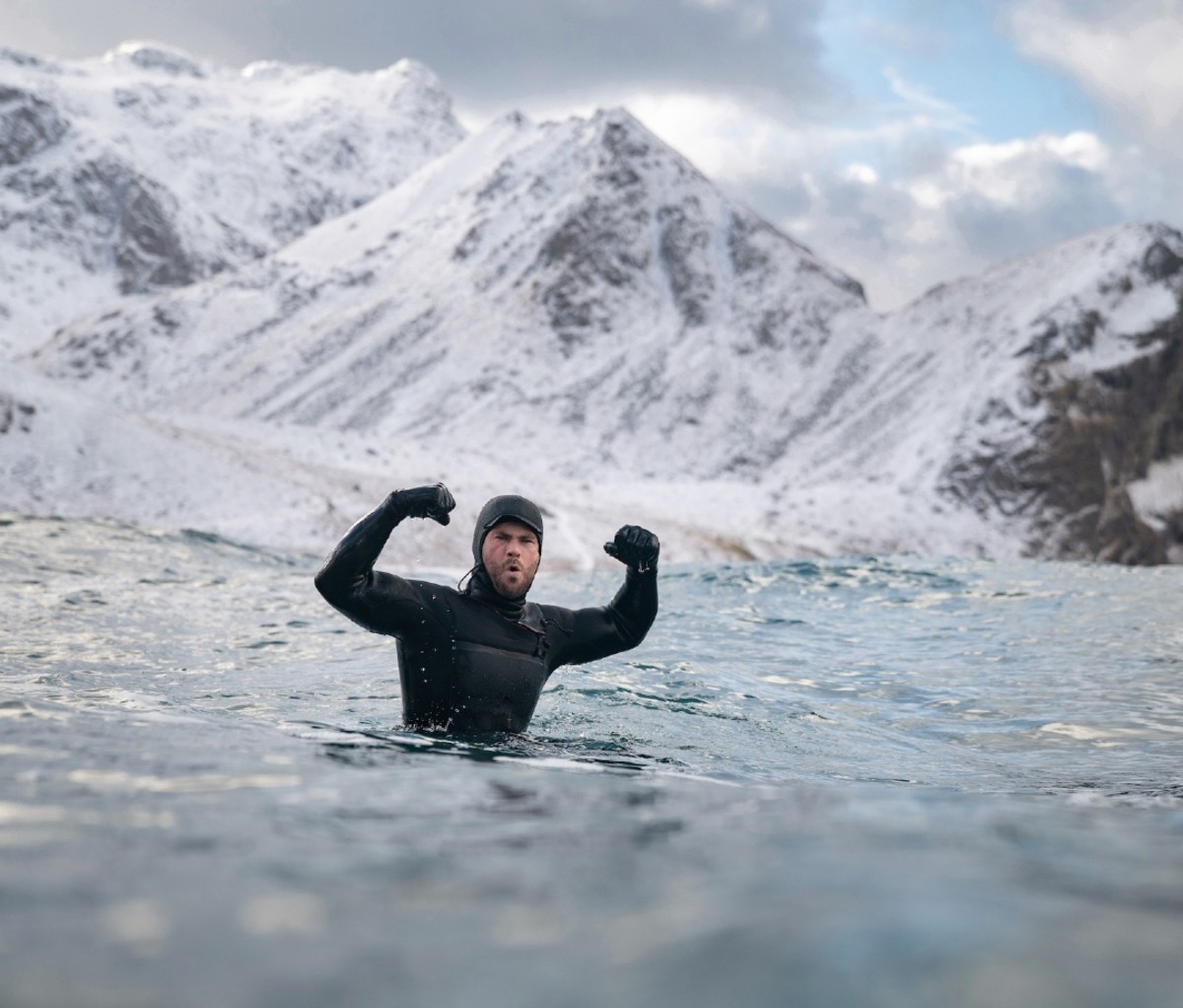 Man celebrating with arms in air while winter surfing in wetsuit