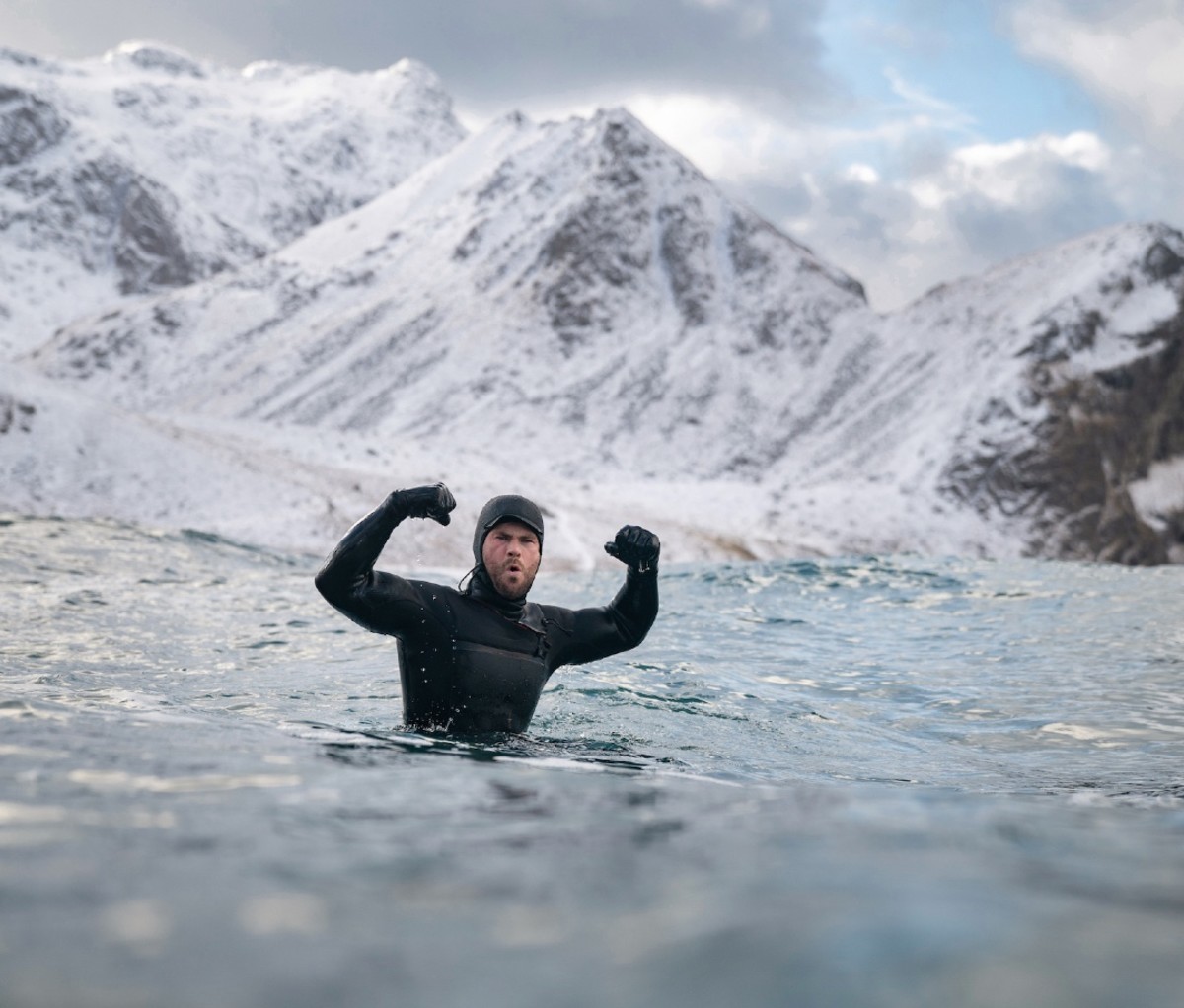 Man celebrating with arms in air while winter surfing in wetsuit