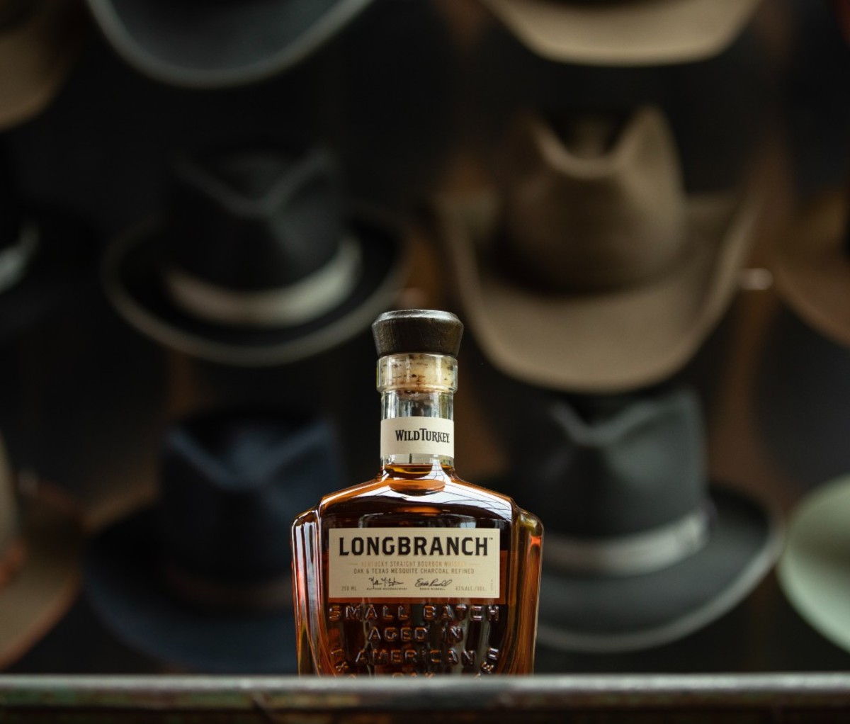 Wall of hats behind bottle of Longbranch whiskey bottle