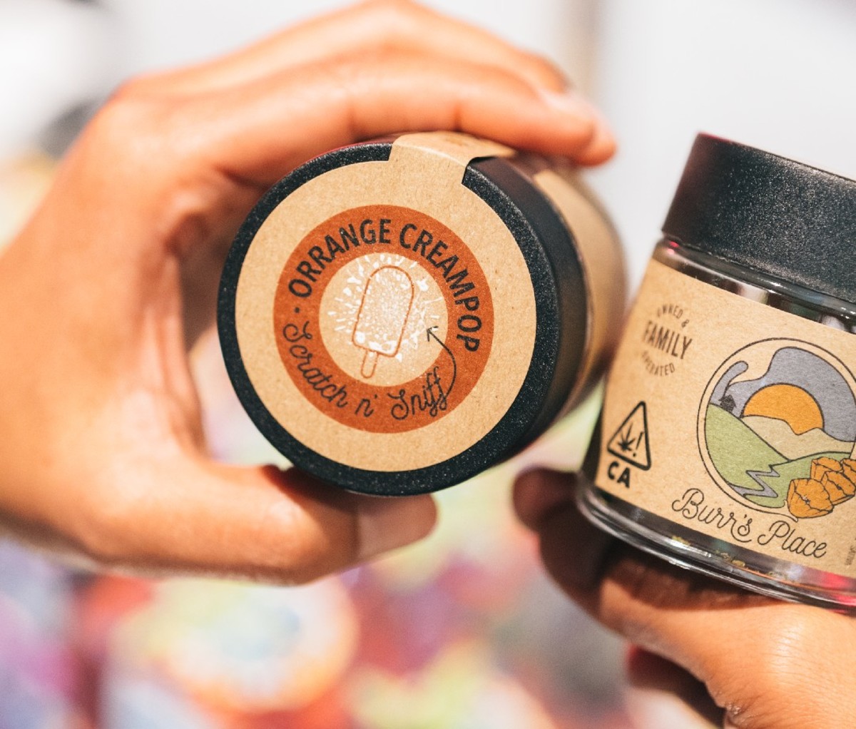 Hand holding a container of cannabis marked with a scratch and sniff sticker.