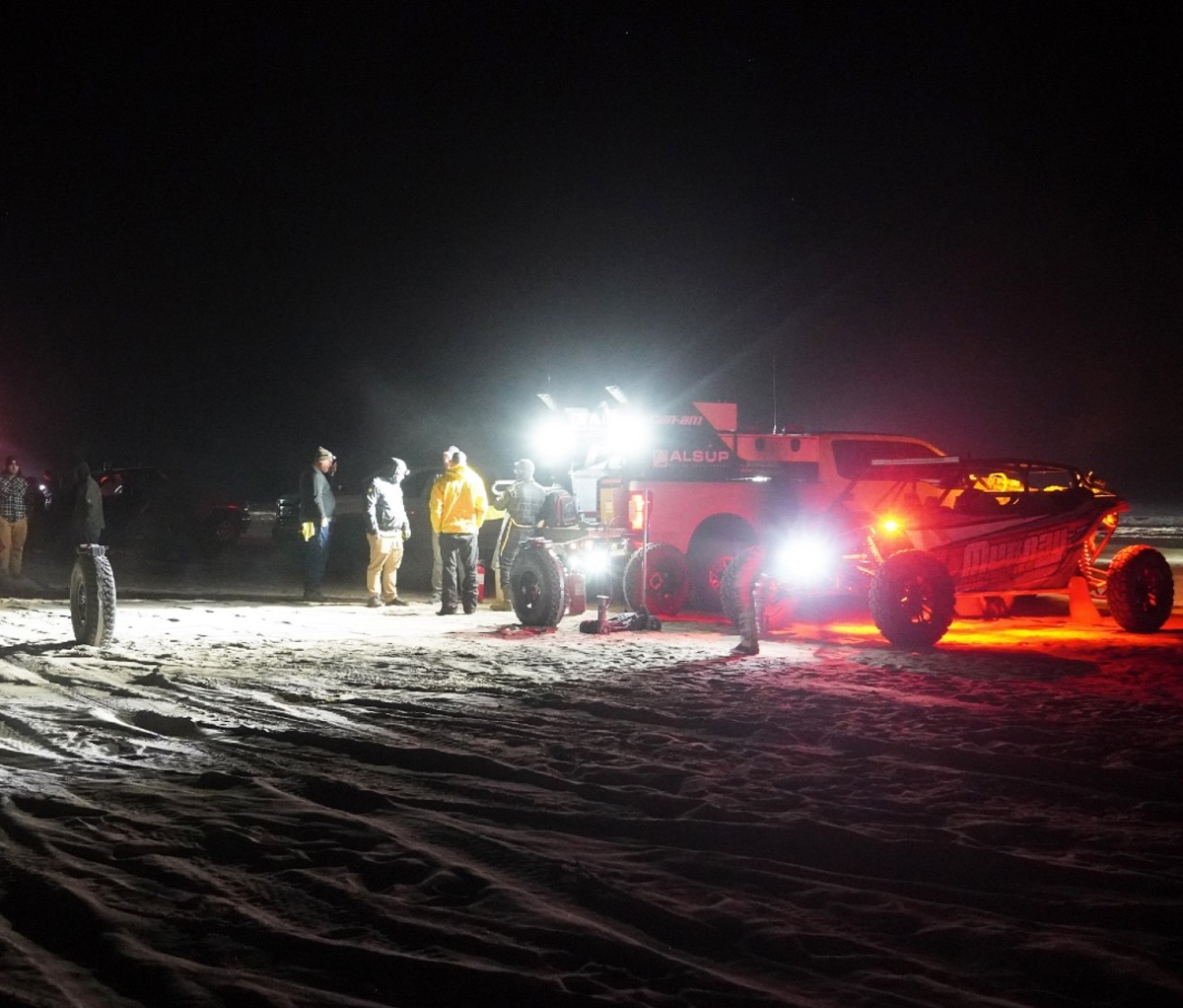 Race car mechanics service a UTV during a pit stop at night in a desert race.