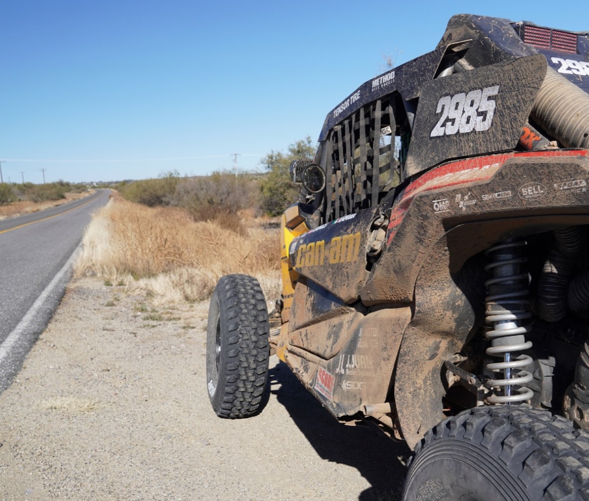 A racing UTV sits by the roadside in the desert.