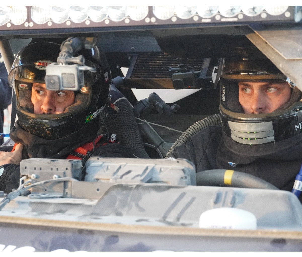 Two desert race car drivers in full gear with serious expressions before an off-road race.