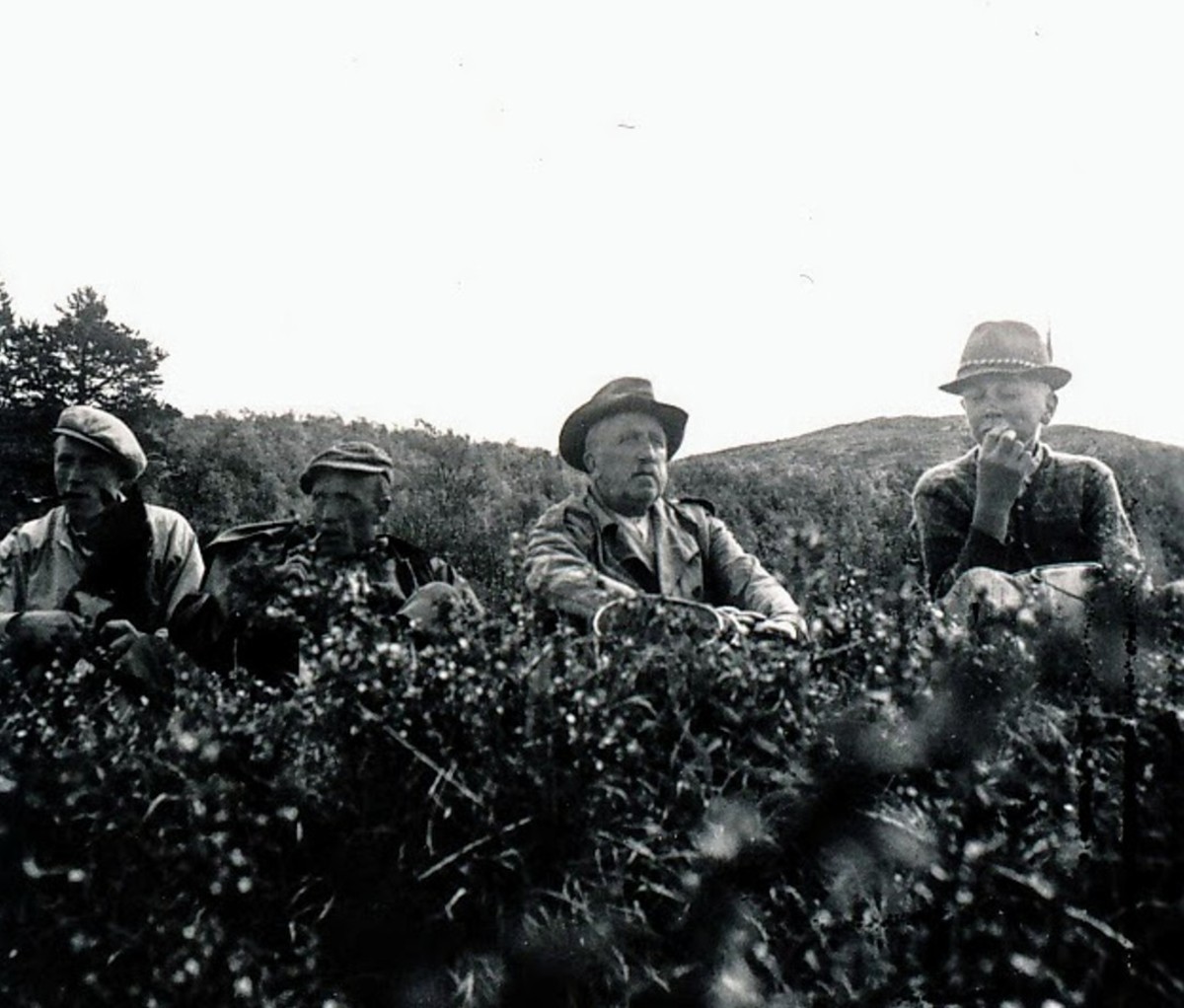 Black and white photo of four men having snack while hiking