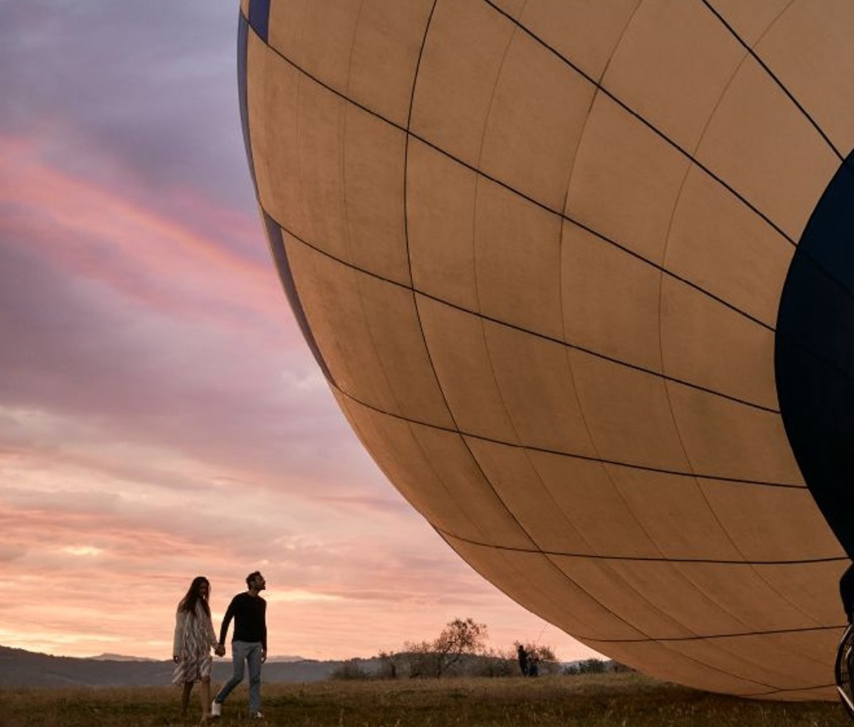 Man and woman holding hands walking toward deflating hot air balloon at sunset