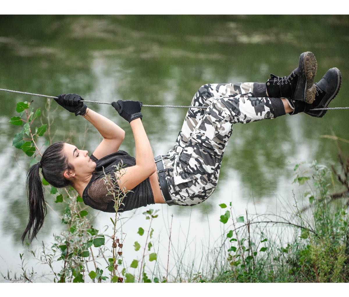 Female soldier climbs across a rope bridge over water.