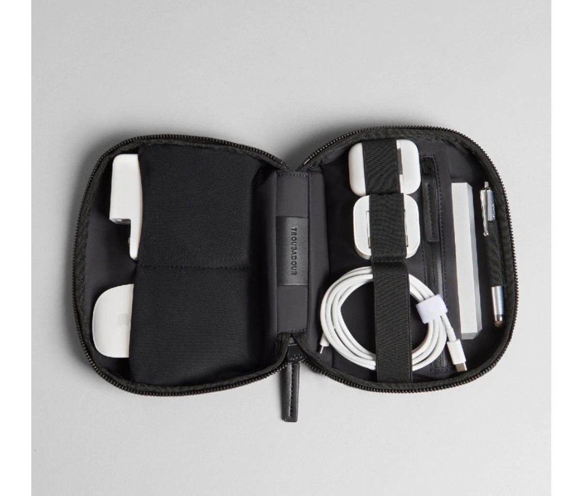 Small black bag open and filled with cables and chargers on an off-white background.