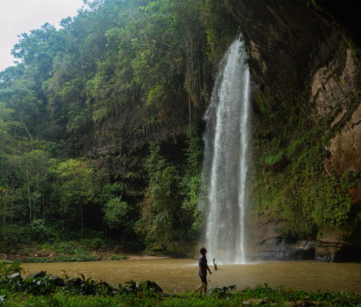 Man walking along a river beside a waterfall.