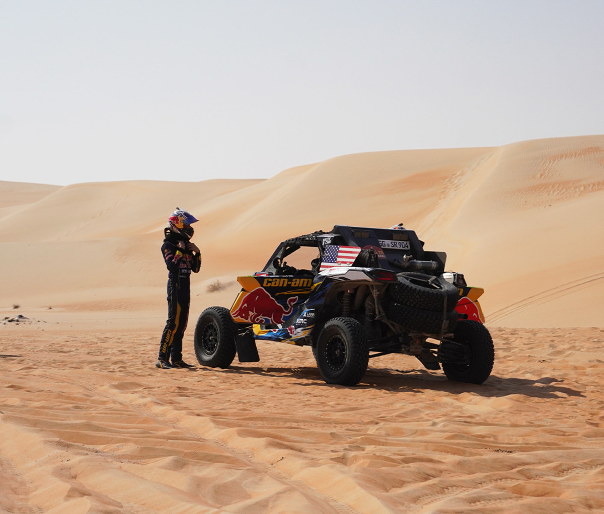 Dakar off-road racer standing next to his side by side with desert dunes in the background.