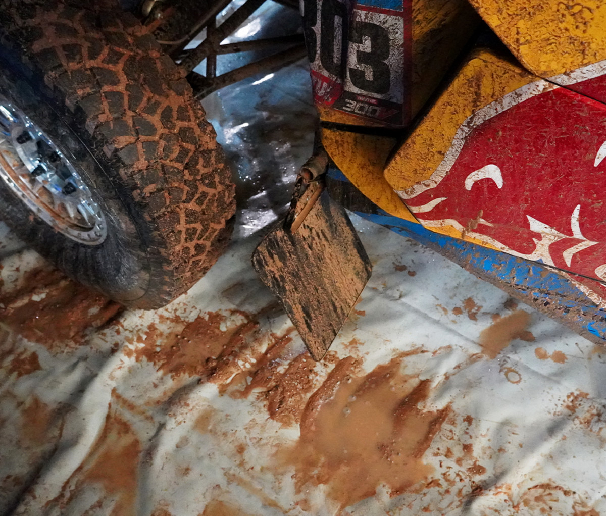 Muddy tire of a Dakar side by side off-roader in front of a muddy mud flap.