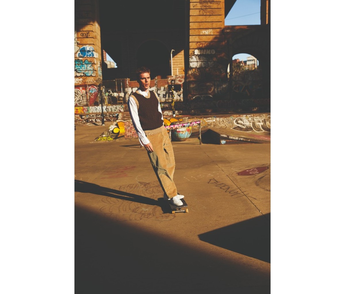 Man wearing a sweater vest and skateboarding.