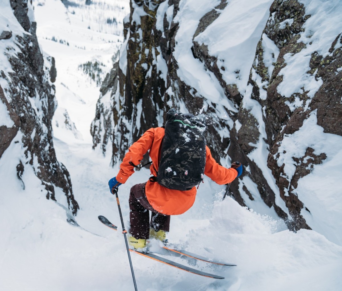 Skier in orange jacket skiing between mountainous boulders
