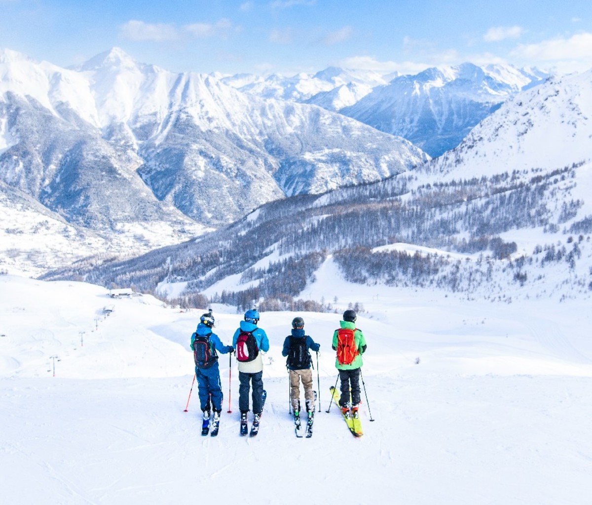 Group of four skiers stading at the top of a run in the alps.