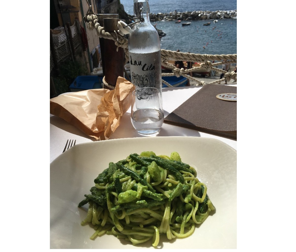 Una ciotola di pasta al pesto che si affaccia sull'acqua.