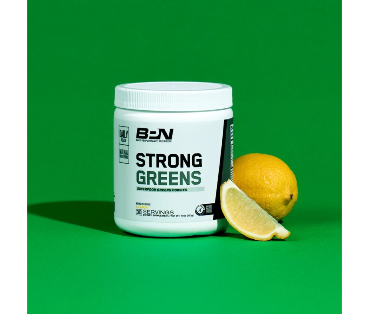 White bottle of greens supplement next to a sliced lemon on a green background.